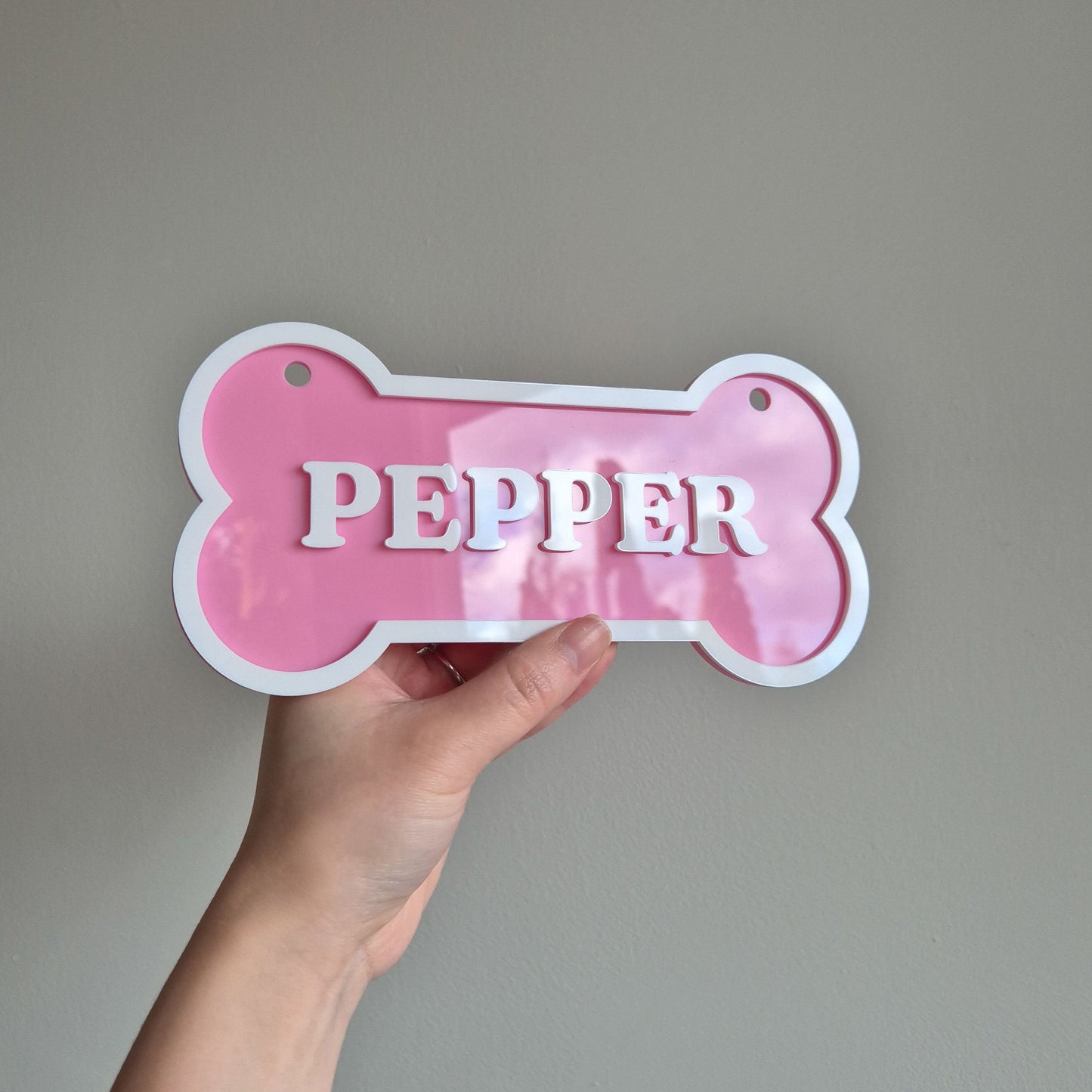 Pink bone-shaped name tag with 'PEPPER' text held against a plain background