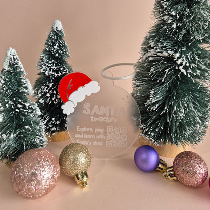 Decorative Christmas ornament with Santa Claus design and festive baubles on a beige background. There is a QR code on the ornament that takes you to Google's Santa Tracker.